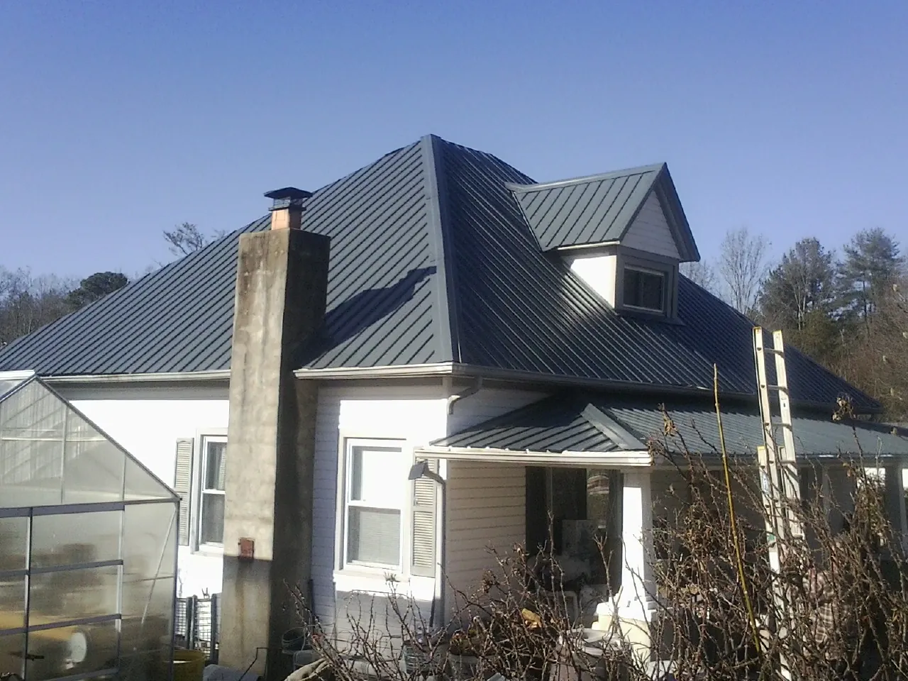 Dark blue standing seam metal roof on a white farmhouse with dormer — Slate & Tile Roof Repair by Roofing Brothers in Galeton