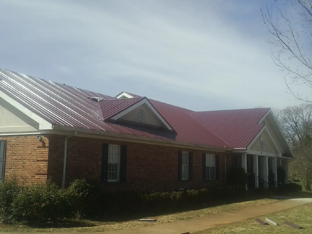 Red metal roof with gabled entries on a long brick building, from a Hail Damage Roof Repair job in Galeton