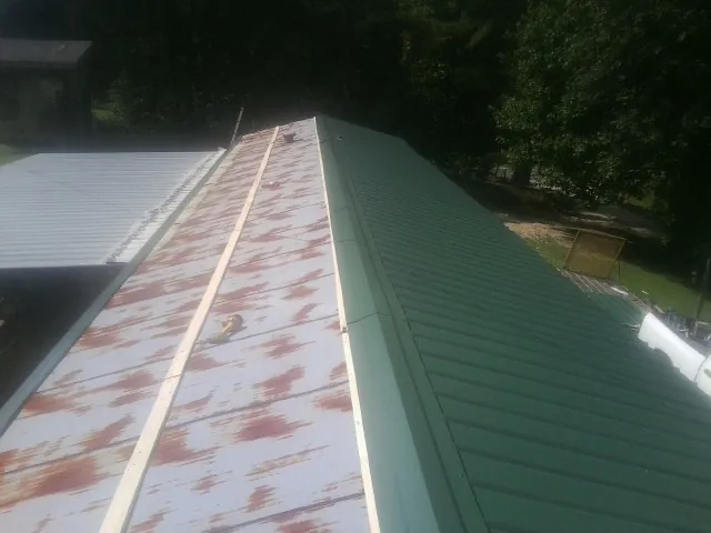 Old rusted panels beside newly installed green metal roofing — Wind Damage Roof Repair by Roofing Brothers in Galeton