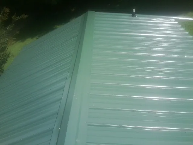New green metal panels meeting at the ridge of a roof — Flat Roof Repair work by our crew in Galeton