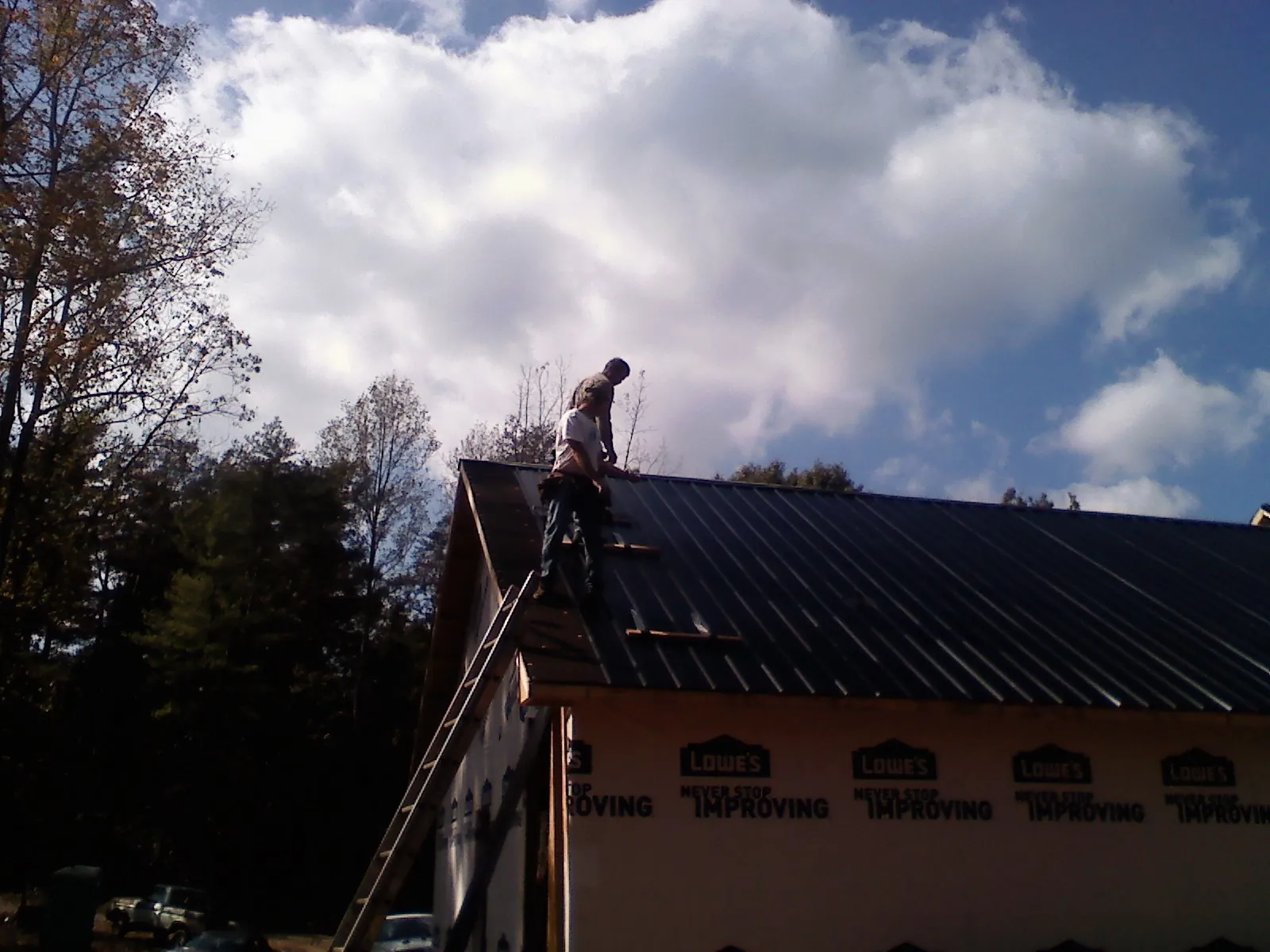 Roofer fastening dark metal panels high against a cloudy sky, from a Roof Inspection job in Galeton