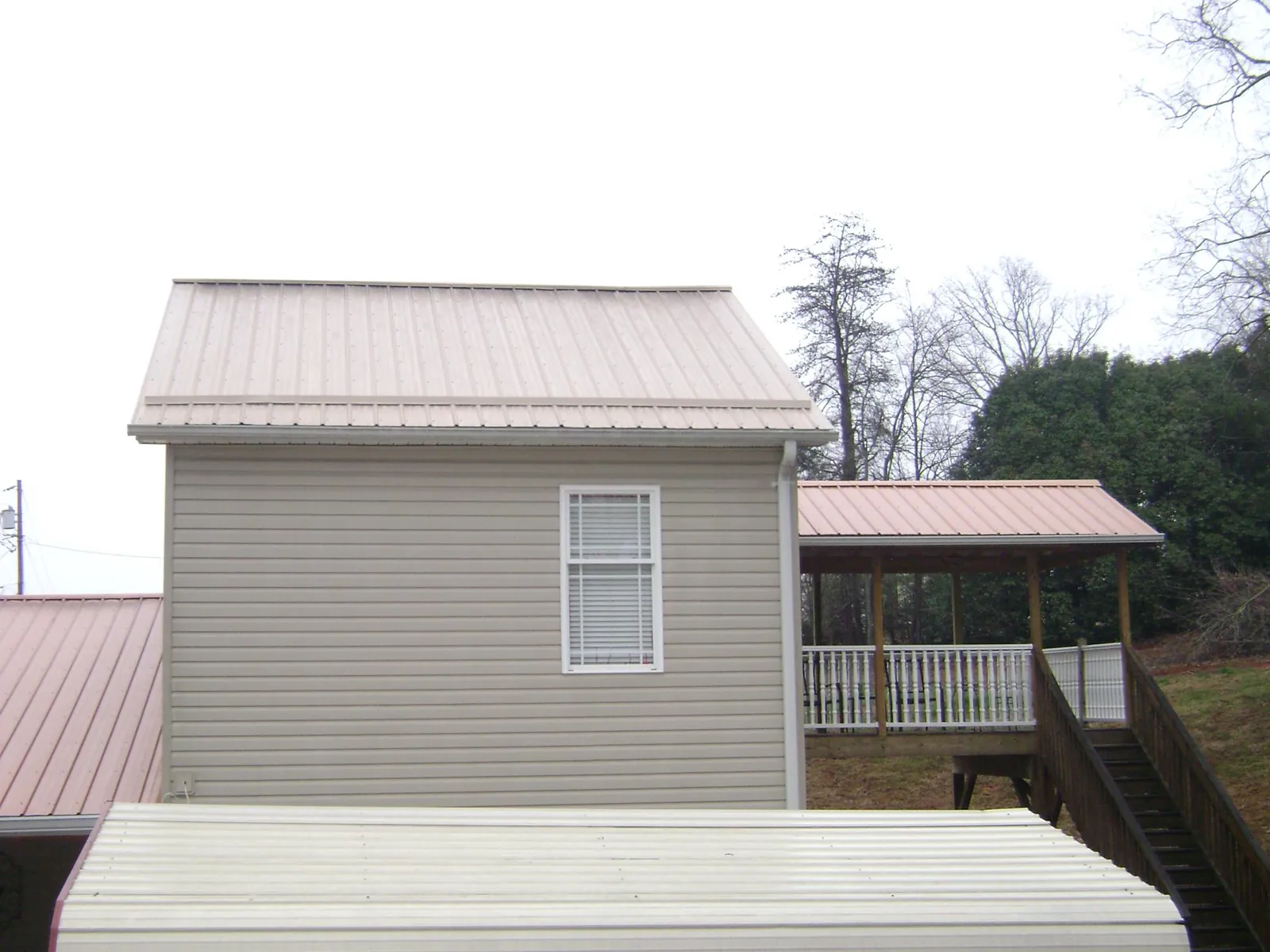 Tan metal roofs on a two story addition and attached porch, from a Roof Replacement job in Galeton